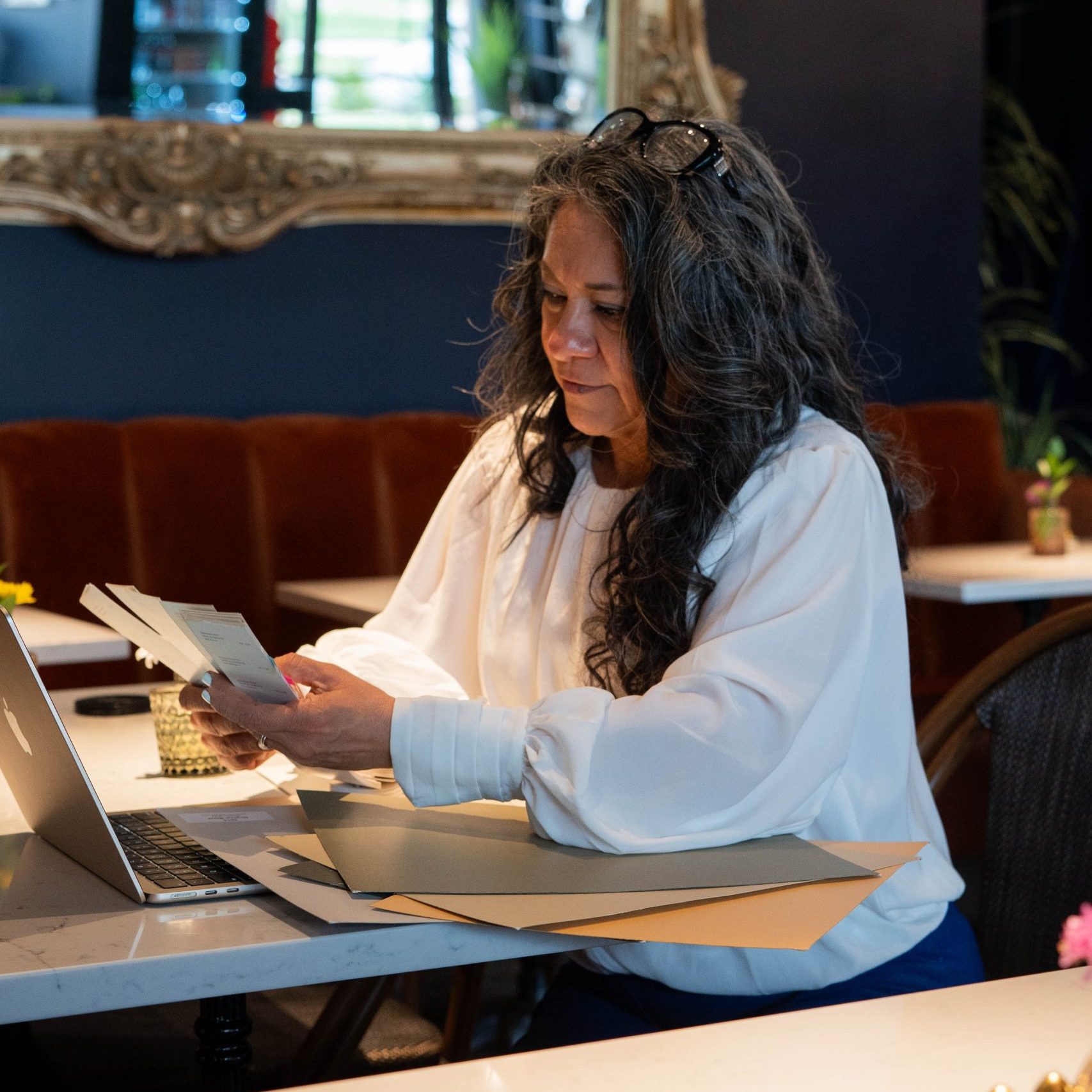 Photo of Sonia, the owner, examining a swatch book in front of a laptop in a restaurant.