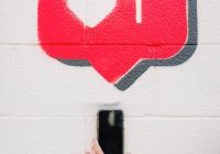 Photo of a hand holding a cell phone in front of a cinder block wall with a speech bubble above it with a hear and #1 inside it to represent the press release section of the site.